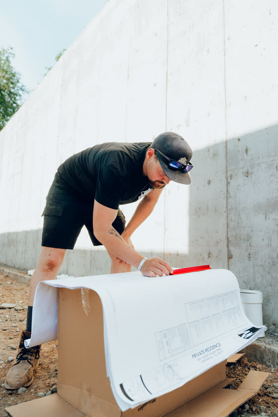 Contractor reviewing blueprints against a poured concrete wall